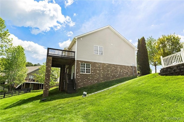 view of side of home with fence, stairs, brick siding, a wooden deck, and a lawn