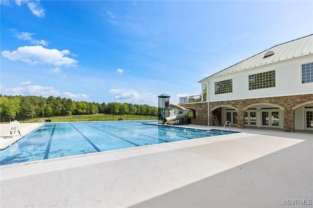 community pool featuring french doors, fence, a water slide, and a patio area