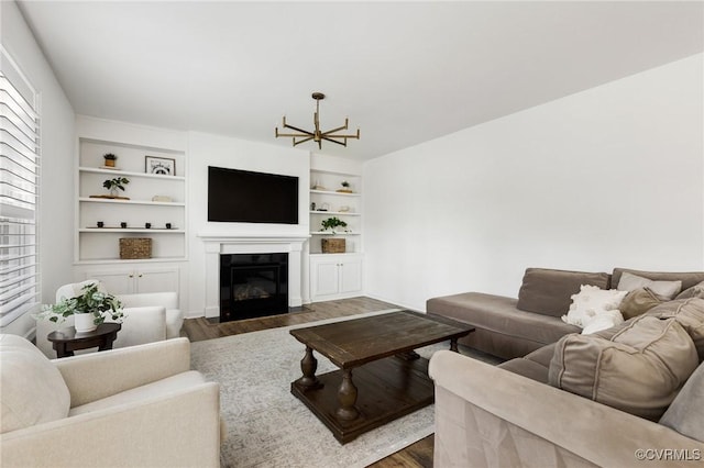 living area with a notable chandelier, a fireplace with flush hearth, built in features, and wood finished floors