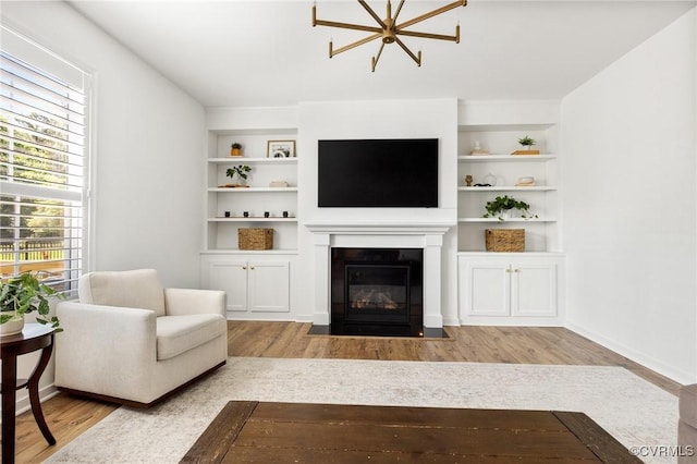 living room featuring a fireplace with flush hearth, built in shelves, and wood finished floors