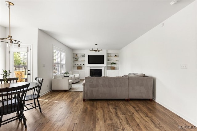 living area with built in features, a fireplace, baseboards, dark wood-style floors, and a notable chandelier