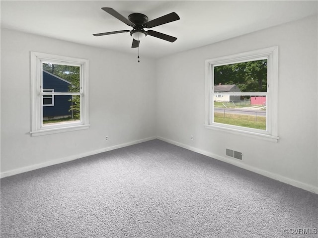 carpeted empty room with ceiling fan, baseboards, visible vents, and a wealth of natural light