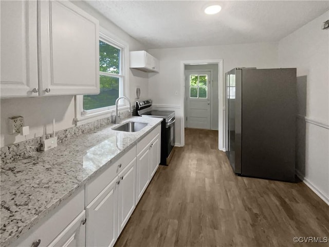 kitchen featuring a healthy amount of sunlight, appliances with stainless steel finishes, wood finished floors, a sink, and white cabinets