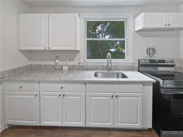 kitchen with a sink, light stone counters, white cabinets, and stainless steel range with electric stovetop