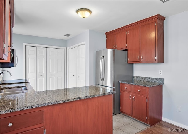 kitchen with a sink, freestanding refrigerator, a peninsula, baseboards, and visible vents