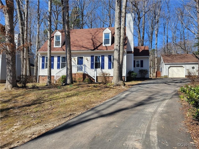 new england style home featuring a garage, aphalt driveway, an outbuilding, and a chimney