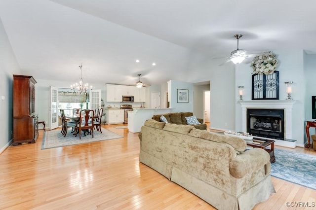 living room with light wood-type flooring, baseboards, a fireplace with raised hearth, ceiling fan with notable chandelier, and lofted ceiling