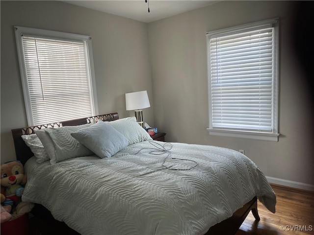 bedroom with wood finished floors, baseboards, and multiple windows