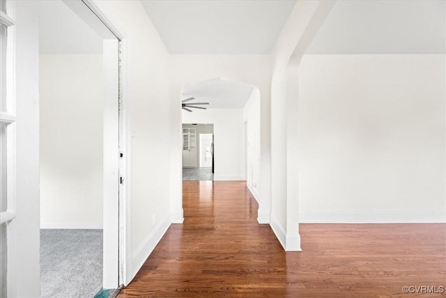 corridor with arched walkways, baseboards, and wood finished floors