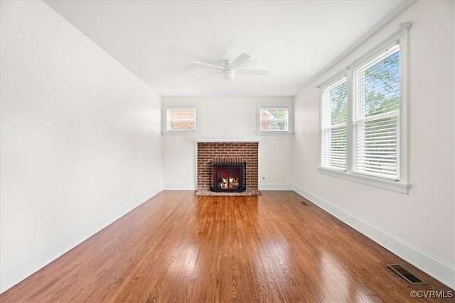 unfurnished living room featuring ceiling fan, visible vents, a fireplace, wood finished floors, and baseboards