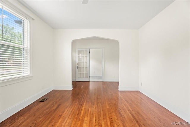 spare room featuring arched walkways, visible vents, a healthy amount of sunlight, and wood finished floors