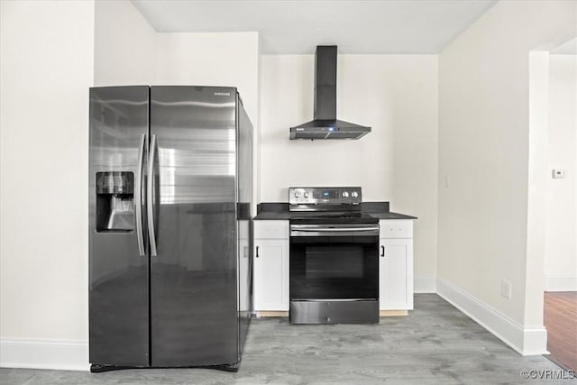 kitchen featuring dark countertops, wall chimney range hood, white cabinets, light wood finished floors, and appliances with stainless steel finishes