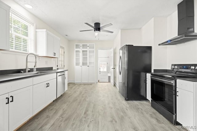 kitchen with a ceiling fan, dark countertops, a sink, stainless steel appliances, and wall chimney exhaust hood