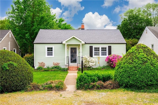 bungalow featuring a shingled roof, a chimney, and a front yard