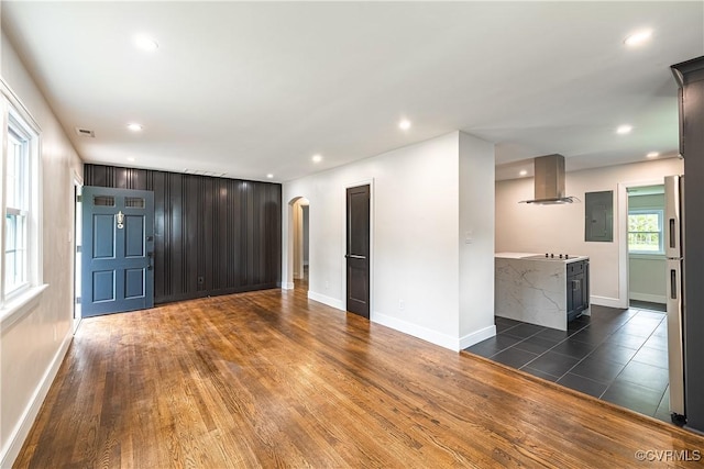 unfurnished living room featuring baseboards, arched walkways, electric panel, and recessed lighting