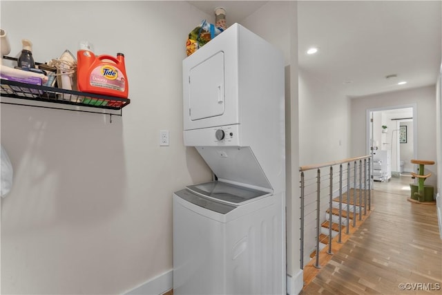 laundry area with recessed lighting, laundry area, stacked washing maching and dryer, and wood finished floors