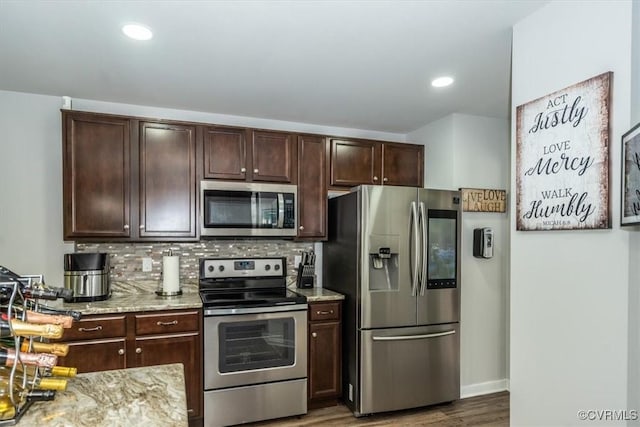 kitchen with decorative backsplash, dark brown cabinetry, wood finished floors, light stone counters, and appliances with stainless steel finishes