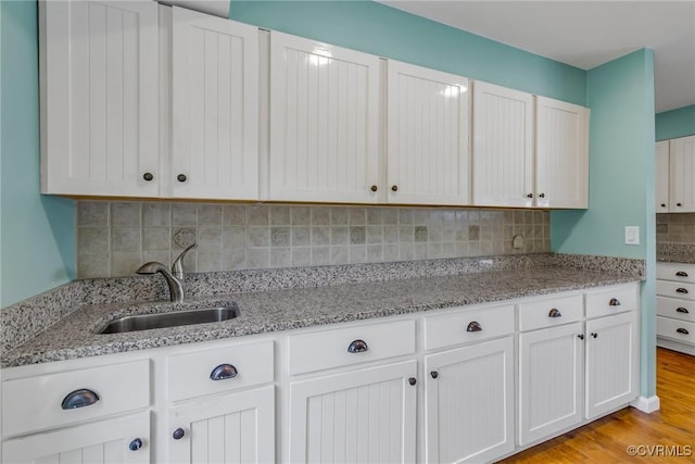 2215 Ditchley Rd, Kilmarnock, VA 22482 - kitchen featuring a sink, tasteful backsplash, white cabinets, light stone counters, and light wood-style flooring