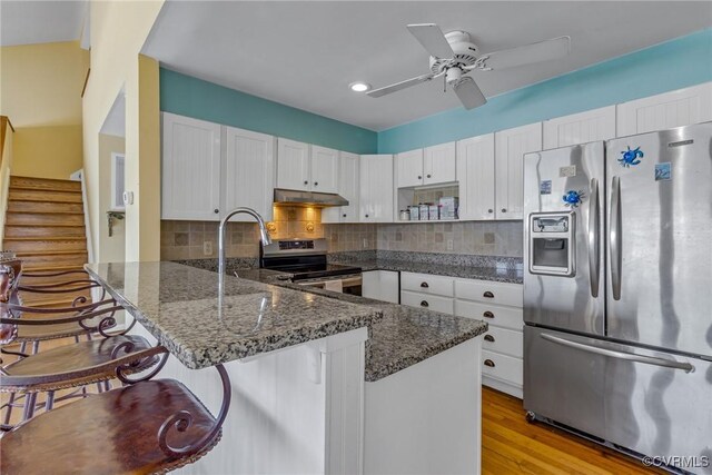 2215 Ditchley Rd, Kilmarnock, VA 22482 - kitchen featuring stainless steel appliances, under cabinet range hood, a peninsula, dark stone countertops, and white cabinets