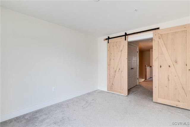 carpeted spare room featuring baseboards and a barn door