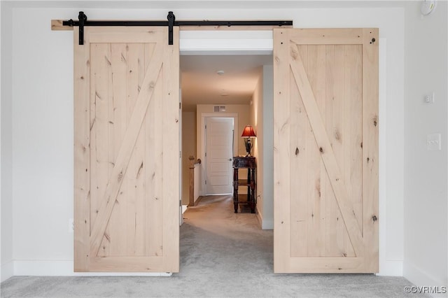 hallway with visible vents, a barn door, baseboards, and carpet flooring