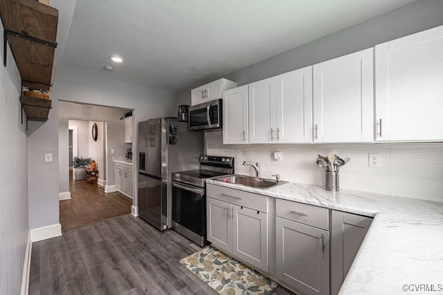 kitchen with appliances with stainless steel finishes, light stone countertops, a sink, baseboards, and dark wood-type flooring