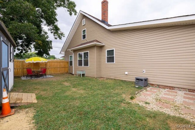 back of property featuring a fenced backyard, a chimney, a lawn, and central AC
