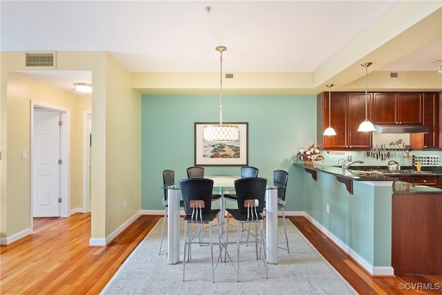 kitchen featuring visible vents, under cabinet range hood, dark countertops, and light wood-type flooring
