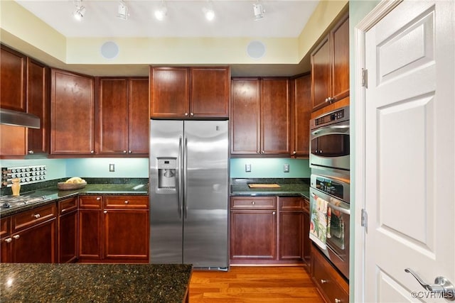 kitchen with dark stone counters, stainless steel appliances, light wood-style flooring, and under cabinet range hood
