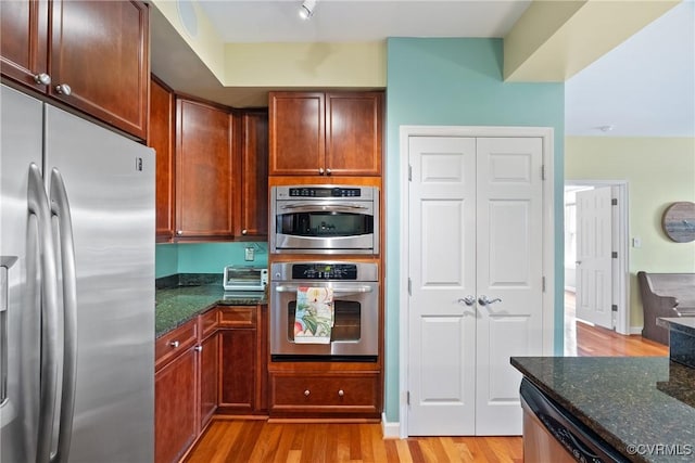 kitchen with light wood-style floors, appliances with stainless steel finishes, a toaster, and dark stone counters