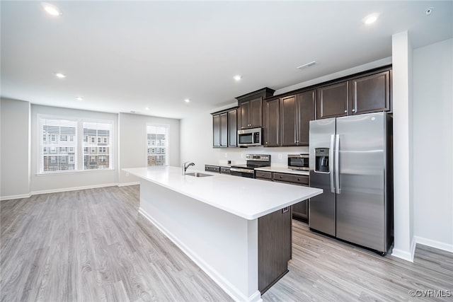 kitchen featuring a sink, light wood finished floors, appliances with stainless steel finishes, and dark brown cabinetry