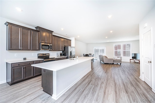 kitchen featuring dark brown cabinetry, appliances with stainless steel finishes, light countertops, a kitchen island with sink, and light wood-style flooring