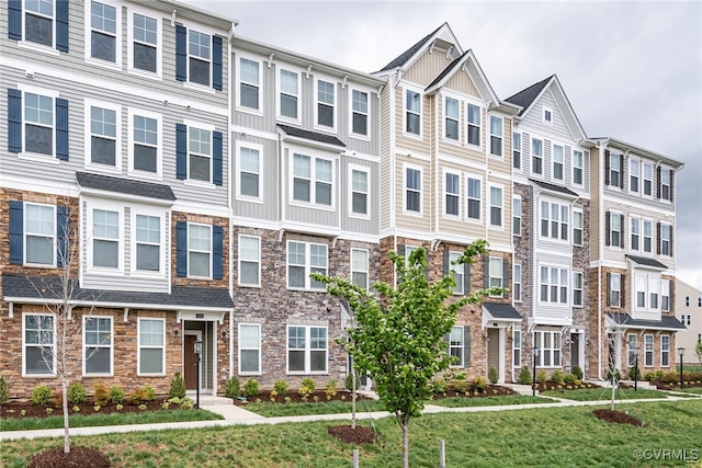 townhome / multi-family property with board and batten siding, stone siding, and a front yard