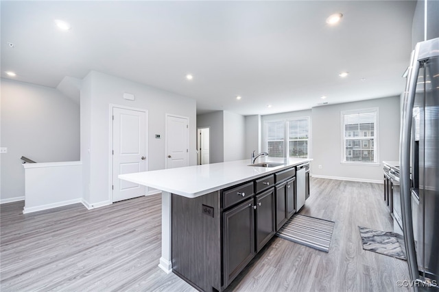kitchen featuring light wood-style floors, light countertops, a center island with sink, and a sink