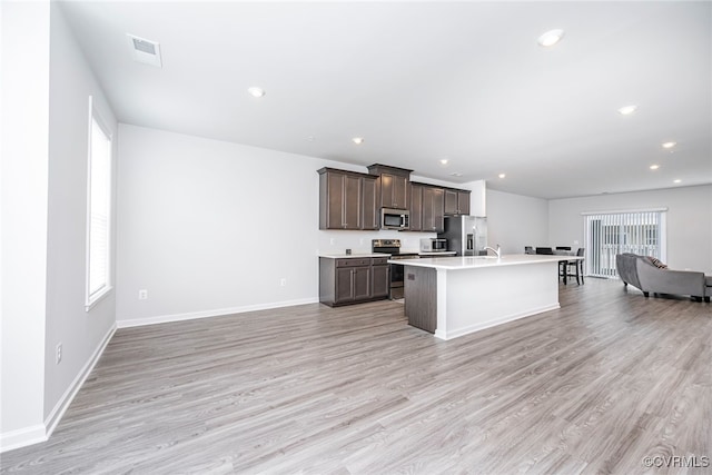 kitchen with open floor plan, appliances with stainless steel finishes, dark brown cabinetry, and a healthy amount of sunlight
