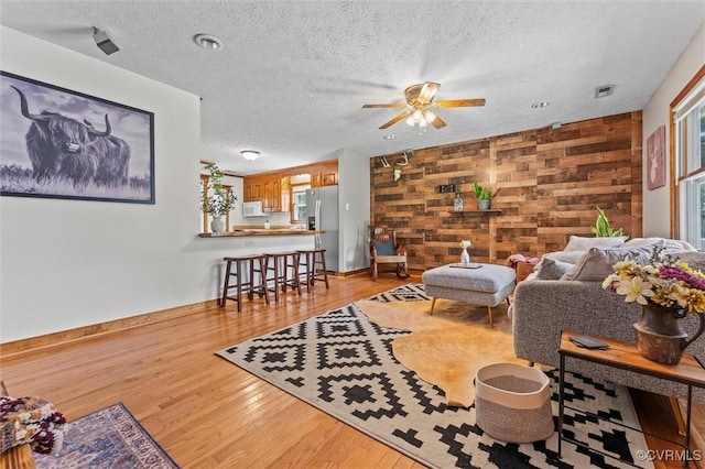 living area featuring ceiling fan, light wood-style floors, wooden walls, a textured ceiling, and an accent wall