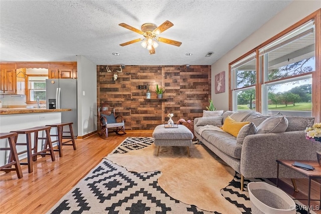 living room with visible vents, light wood-style flooring, ceiling fan, and a textured ceiling