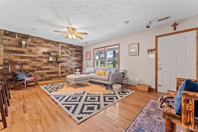 living area featuring ceiling fan, wood finished floors, a textured ceiling, baseboards, and wooden walls