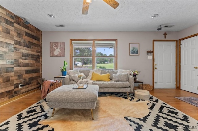 living room featuring wood walls, wood finished floors, a textured ceiling, and a ceiling fan