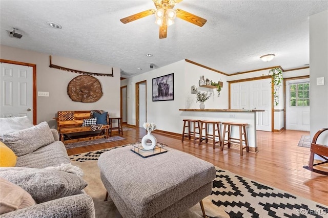 living area with a textured ceiling, baseboards, light wood-type flooring, and a ceiling fan