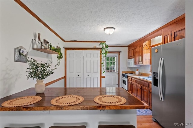 kitchen with appliances with stainless steel finishes, ornamental molding, a kitchen bar, brown cabinetry, and a textured ceiling
