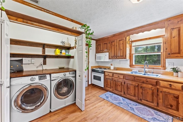 interior space with washing machine and dryer, a sink, light wood-type flooring, a textured ceiling, and white appliances