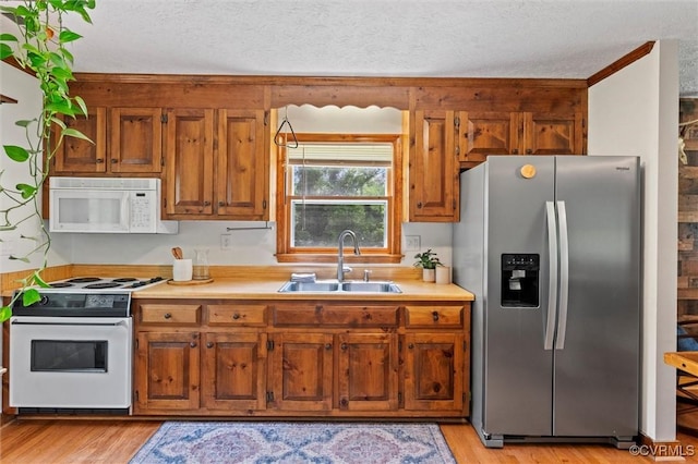 kitchen featuring a textured ceiling, brown cabinetry, white appliances, a sink, and light countertops
