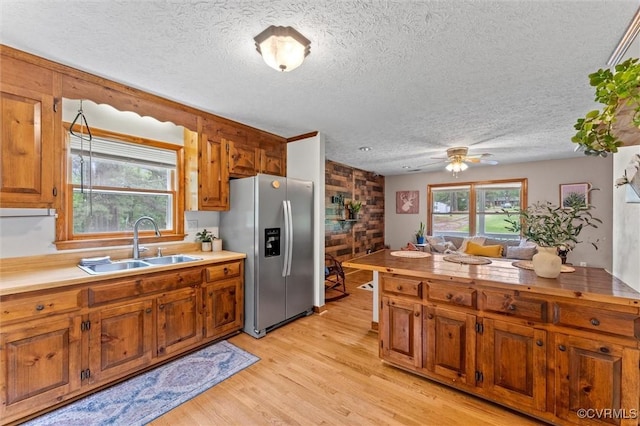 kitchen with stainless steel fridge with ice dispenser, a sink, brown cabinets, a textured ceiling, and light wood finished floors