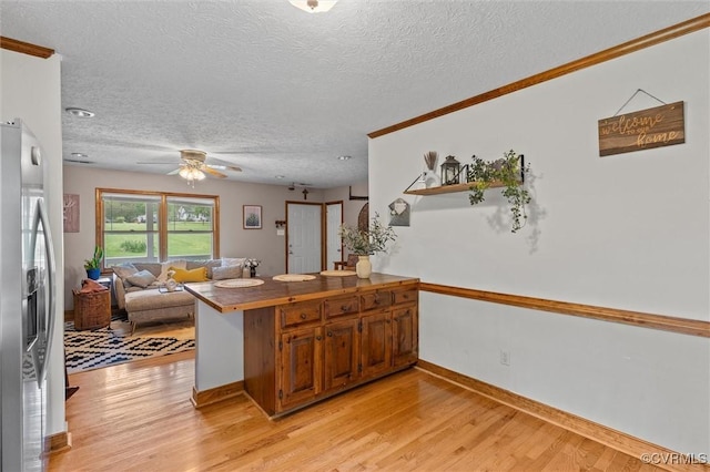 kitchen with a peninsula, brown cabinets, a textured ceiling, stainless steel refrigerator with ice dispenser, and open floor plan