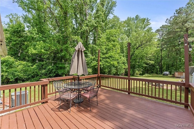 deck with outdoor dining area, a lawn, and cooling unit