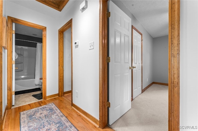 hallway featuring baseboards, light wood-style flooring, and a textured ceiling