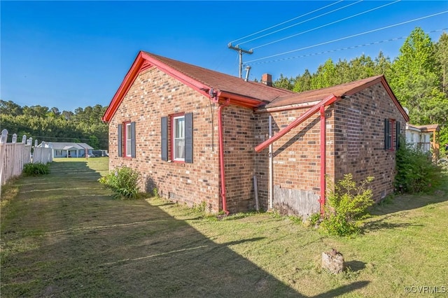 view of home's exterior with brick siding, fence, and a yard