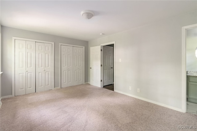 unfurnished bedroom featuring ensuite bathroom, carpet flooring, baseboards, and two closets