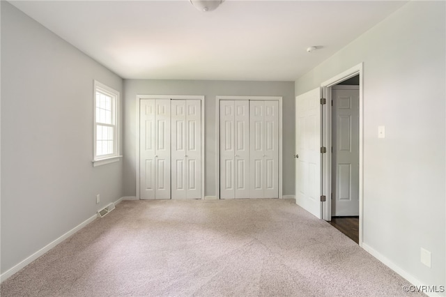 unfurnished bedroom featuring visible vents, carpet, multiple closets, and baseboards